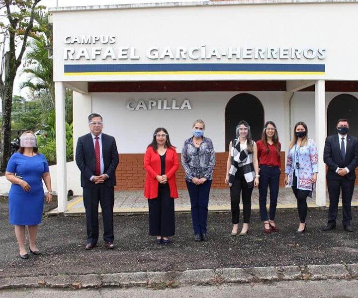 6 Administrativos y los dos pares académicos en una foto grupal, en una sola línea guardando la distancia, con tapabocas y mascarillas. Están ubicados en el campus universitario de Galicia, frente a la capilla de la Institución.