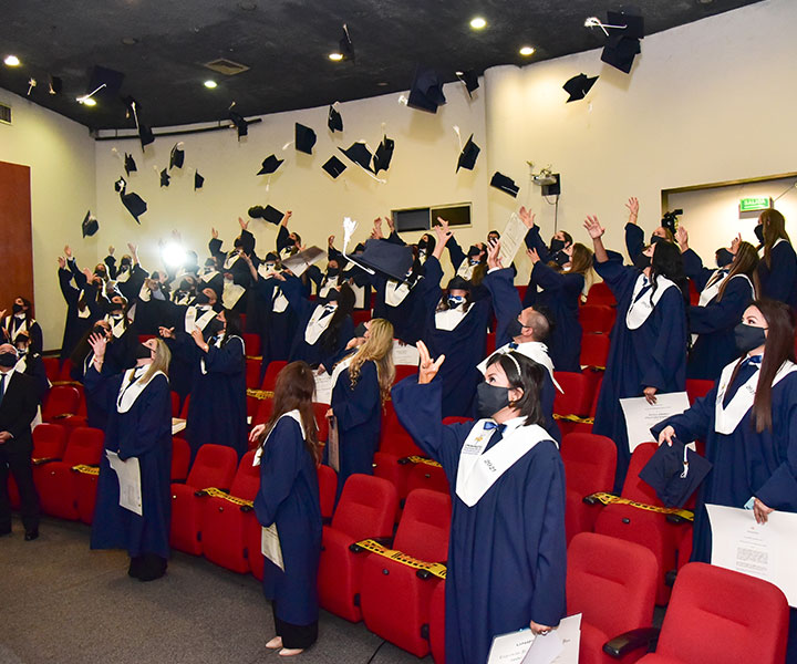 Personas de pie en auditorio vistiendo togas de color azul lanzando el birrete como graduados muy felices 