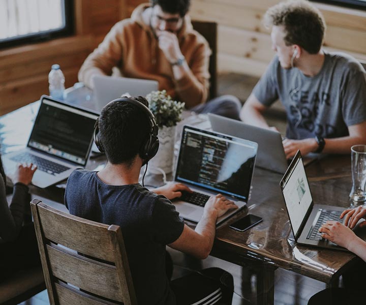 Cuatro estudiantes reunidos  en una mesa, cada uno con un computador estudiando