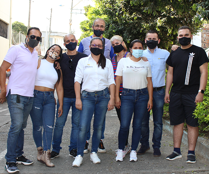 Grupo de 9 voluntarios y beneficiarios, en grupo. Mirando a la cámara en un plano general de pies a cabeza.