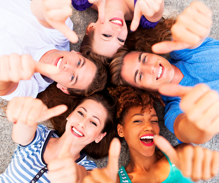 Jóvenes acostados en círculo sonriendo  y haciendo la seña de bien (pulgar arriba)