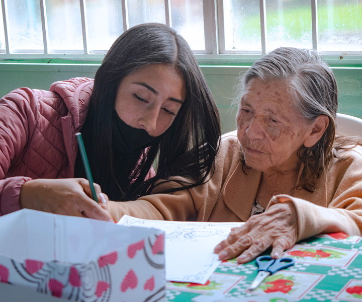 Estudiante UNIMINUTO enseñando a escribir a abuelita