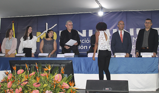 Estudiante recibiendo su certificado de beca de la mesa principal de UNIMINUTO