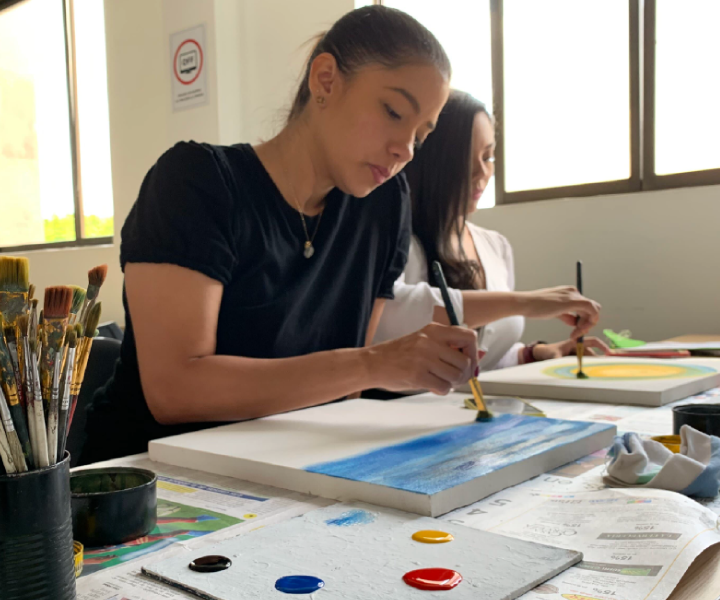 Estudiantes mujeres pintando en un lienzo.