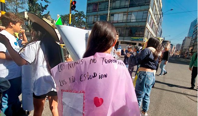 Participante del Tercer Carnaval por los Derechos de las Infancias iluminando con pancarta las calles de la localidad de los Mártires.