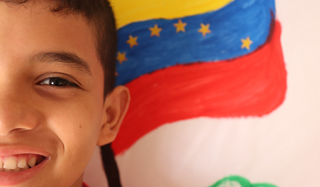 Niño migrante con fondo de la bandera de Venezuela.