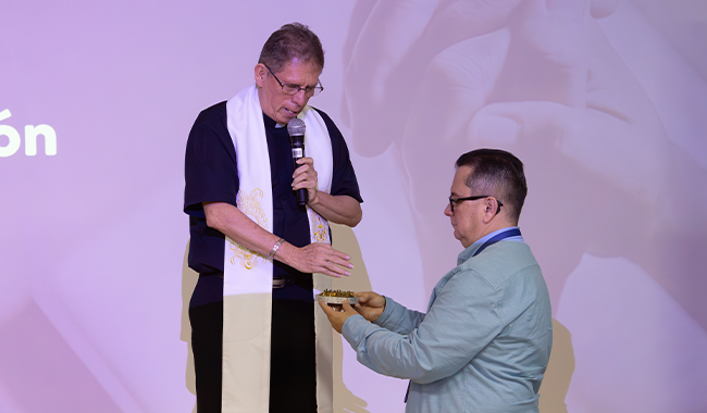 Padre realizando oración de apertura y bendiciendo insignia de la Cruz del Minuto de Dios a entregar. 