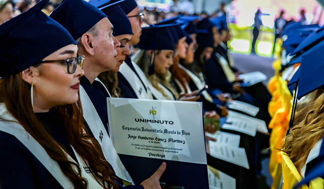 Estudiantes con toga y birrete sosteniendo sus diplomas en la ceremonia de grados. 