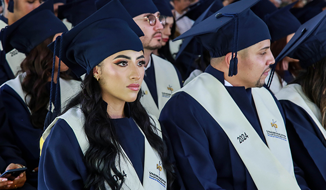 Estudiantes sentados con toga y birrete, prestando atención a la ceremonia de graduación.