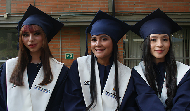 Tres estudiantes con toga y birrete en la ceremonia de certificación de UNIMINUTO