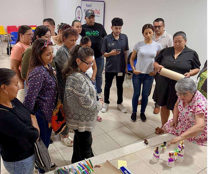 Varias personas están de pie alrededor de una mesa, con una mujer en el medio, creando un ambiente de discusión y colaboración.