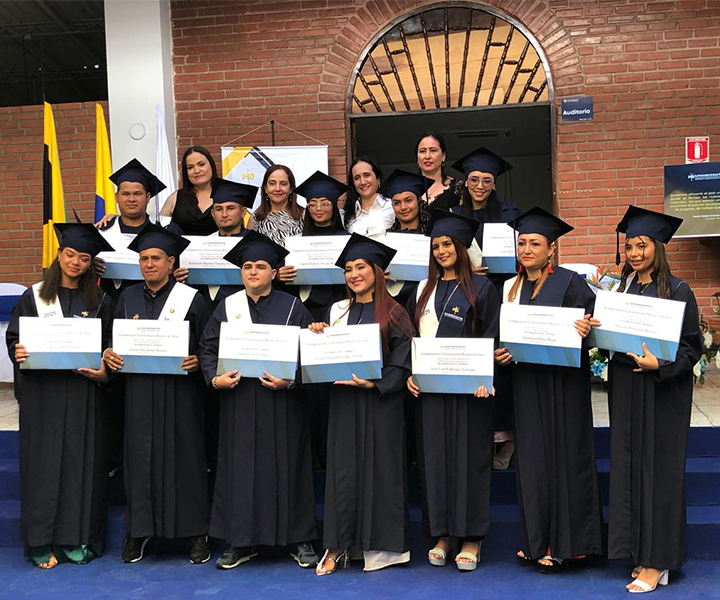 Grupo de graduandos posando con sus diplomas, acompañados por docentes, todos vestidos con toga y birrete.