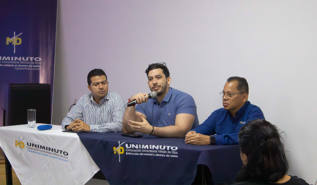 Mesa principal del IX Coloquio de Posgrados con José Albeiro Tamara, Brian Bustos y José Alberto Cristancho; Brian Bustos habla al público con un micrófono