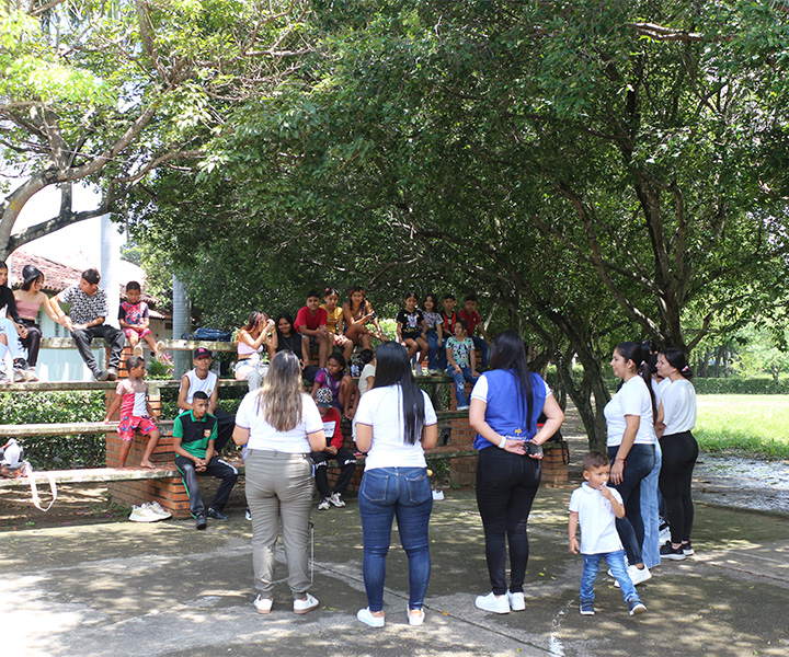Un grupo de personas, incluidos niños, participan en una actividad grupal al aire libre, dirigida por docentes y estudiantes de Trabajo Social
