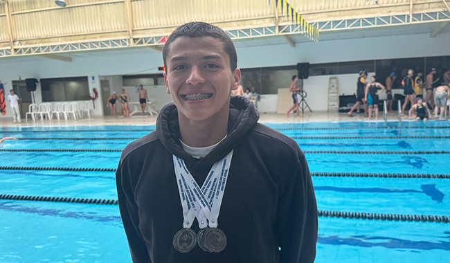 Estudiante campeón en natación posando con 4 medallas