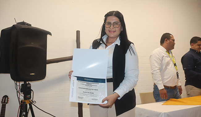 Mujer sostiene su certificado frente a una cámara durante la ceremonia de graduación del curso de drones.
