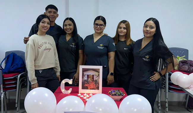 rupo de estudiantes posando junto a una decoración con globos blancos y rojos en forma de corazón.