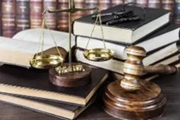 Balanza de la justicia junto a un mazo de juez sobre una mesa, con un reloj de arena y libros de derecho al fondo, representando el concepto de ley, justicia y paso del tiempo en los procesos legales.