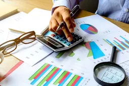 imagen de manos marcado una calculadora con una lupa 