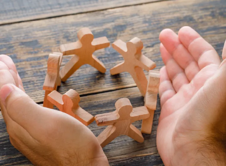 Manos al rededor de un grupo de figura de maderas en alusión a equipo