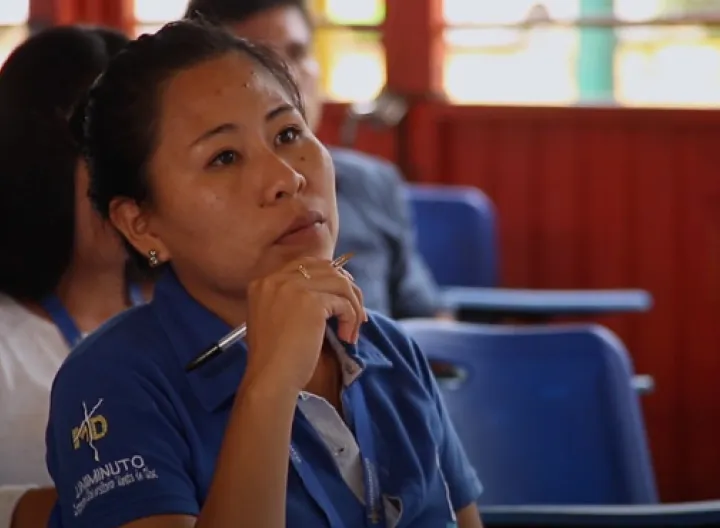 Estudiante en un salón de clases, con esfero en la mano, prestando atención a lo que están explicando