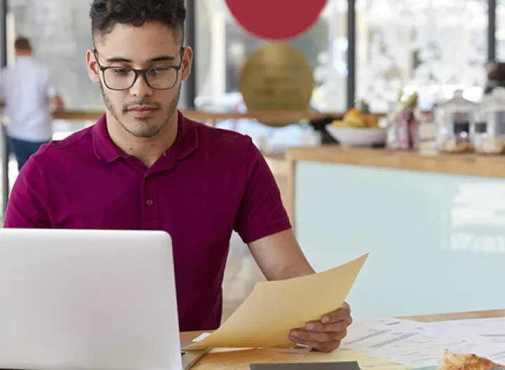 Hombre joven camiseta vino tinto sentado en un escritorio con un computador. 