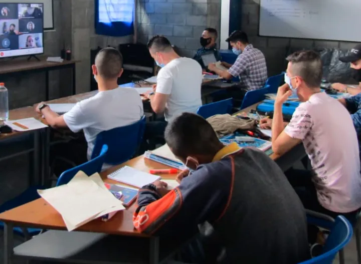 hombres en aula de clase observando videoconferencia en computador.