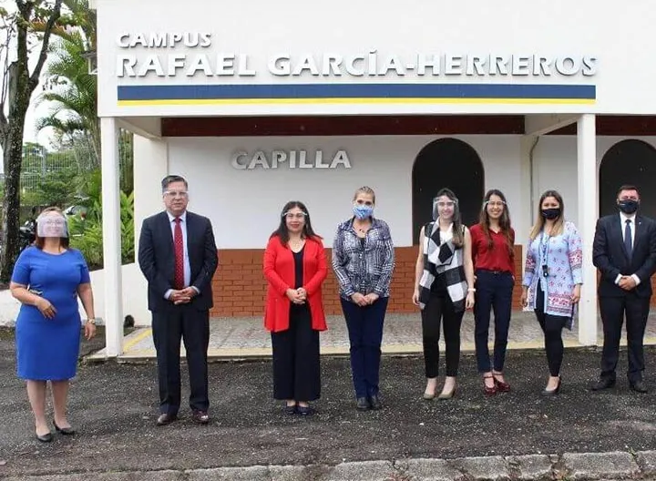 6 Administrativos y los dos pares académicos en una foto grupal, en una sola línea guardando la distancia, con tapabocas y mascarillas. Están ubicados en el campus universitario de Galicia, frente a la capilla de la Institución.