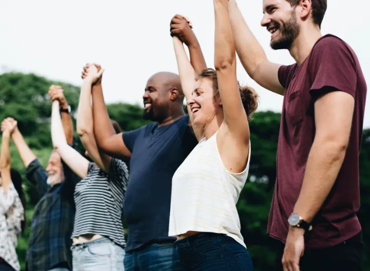 Personas en campo abierto cogidos de la mano, levantan sus brazos.