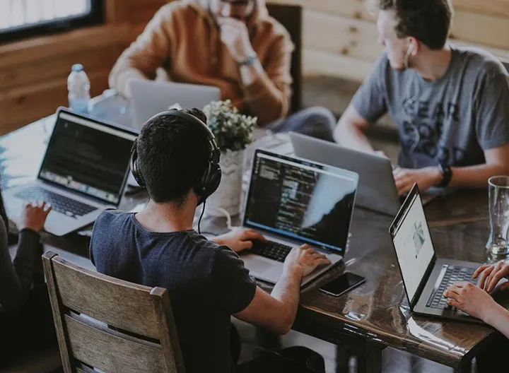 Cuatro estudiantes reunidos  en una mesa, cada uno con un computador estudiando