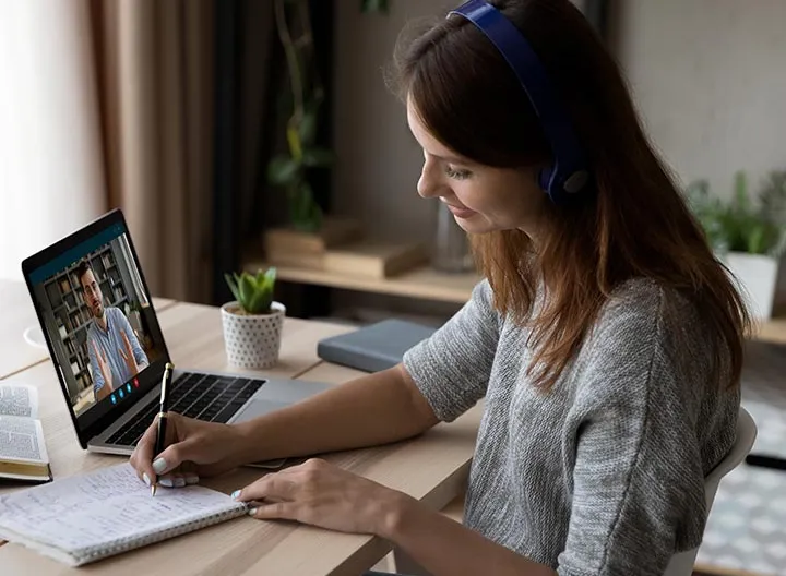 Persona usando audífonos  tomando nota en una reunión virtual.