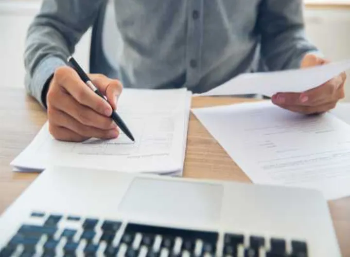 Persona firmando documentos frente a computador