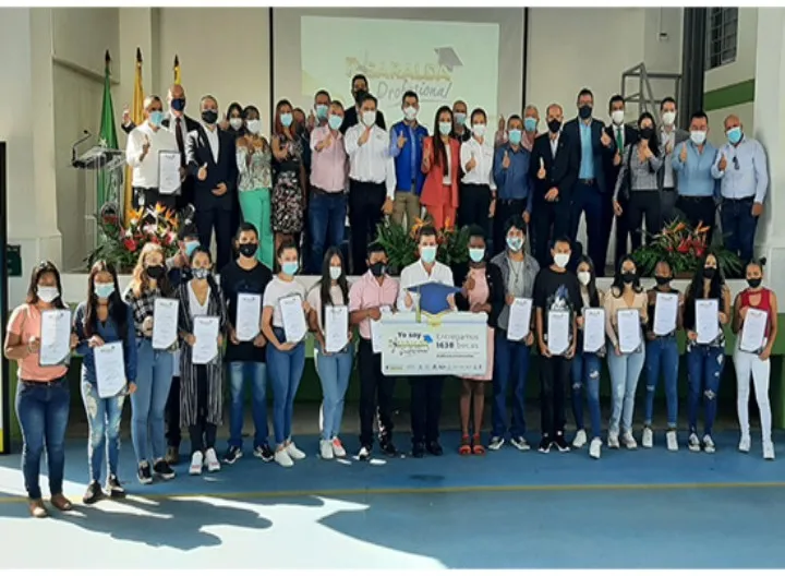 En una cancha, con fondo vegetal. Presencia de la directora académica, una chica beneficiaria de la beca y el secretario de gobierno sostienen un cartel que dice entregamos 1638 becas. El  cartel tiene undiseño horizontal y un birrete azul. 