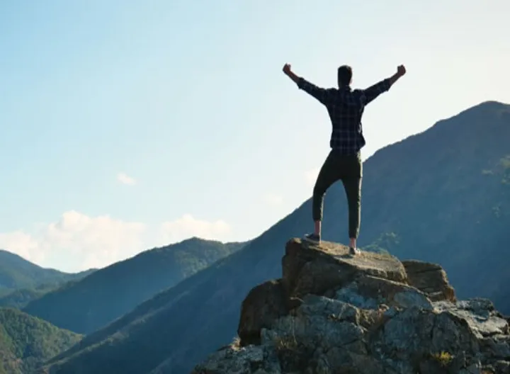 hombre en la cima de una montaña extendiendo sus brazos