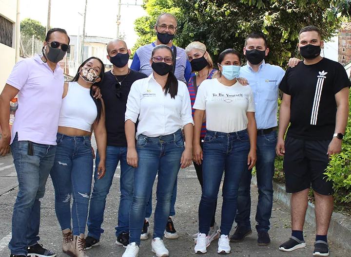 Grupo de 9 voluntarios y beneficiarios, en grupo. Mirando a la cámara en un plano general de pies a cabeza.