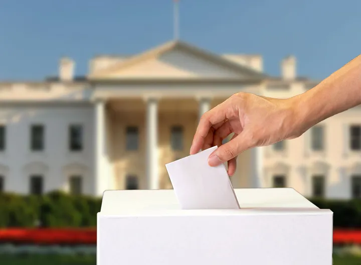 Mano depositando su tarjetón electoral frente a la casa blanca. 