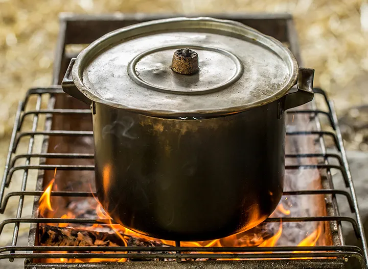 Olla de metal con tapa sobre una parrilla de hierro sobre un fuego generado por una estufa ecológica