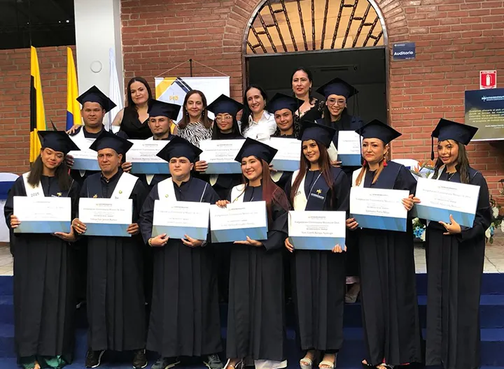 Grupo de graduandos posando con sus diplomas, acompañados por docentes, todos vestidos con toga y birrete.