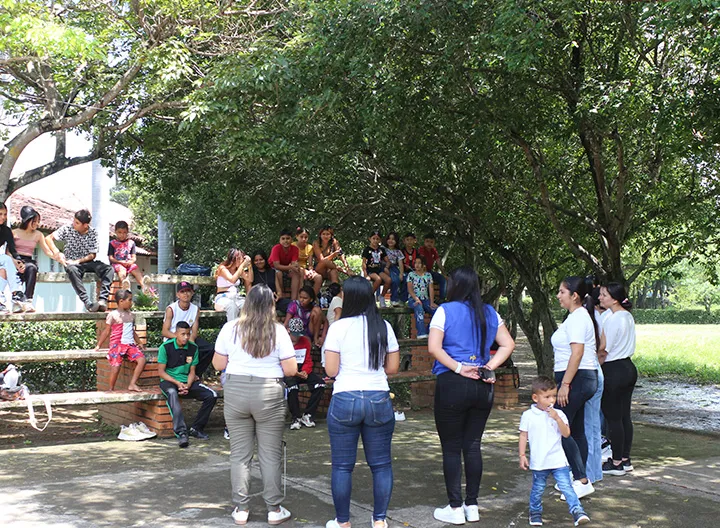 Un grupo de personas, incluidos niños, participan en una actividad grupal al aire libre, dirigida por docentes y estudiantes de Trabajo Social