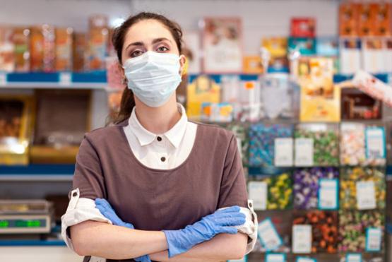 Mujer cruzada de brazos con tapabocas y guantes, de fondo se ve una papelería