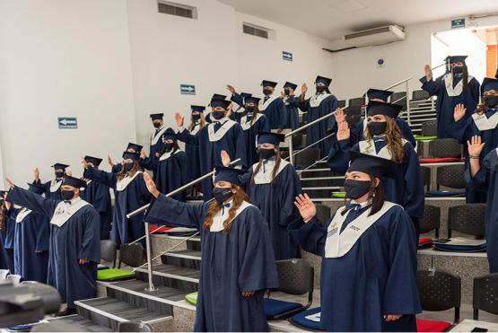 Estudiantes de píe usando toga azul con la mano derecha levantada haciendo juramento de grado 