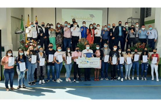 En una cancha, con fondo vegetal. Presencia de la directora académica, una chica beneficiaria de la beca y el secretario de gobierno sostienen un cartel que dice entregamos 1638 becas. El  cartel tiene undiseño horizontal y un birrete azul. 