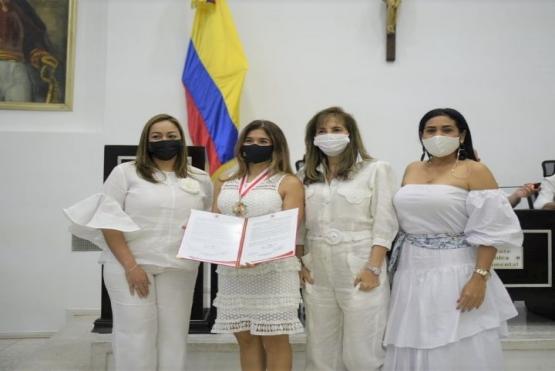 Cuatro mujeres vestidas de blanco una tiene una medalla y pergamino de reconocimiento