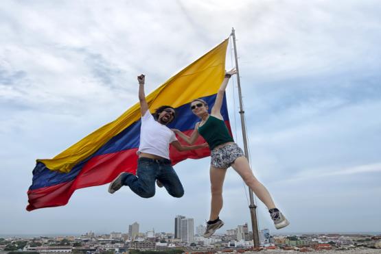 Jovenes saltando frente a una bandera de Colombia