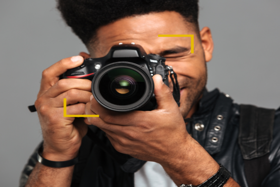 Joven sosteniendo una cámara de fotografía profesional sobre su rostro. 