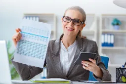 Mujer sentada en escritorio con documento y calculadora en la mano