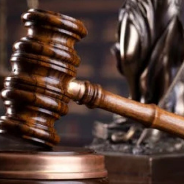 Balanza de la justicia junto a un mazo de juez sobre una mesa, con un reloj de arena y libros de derecho al fondo, representando el concepto de ley, justicia y paso del tiempo en los procesos legales.
